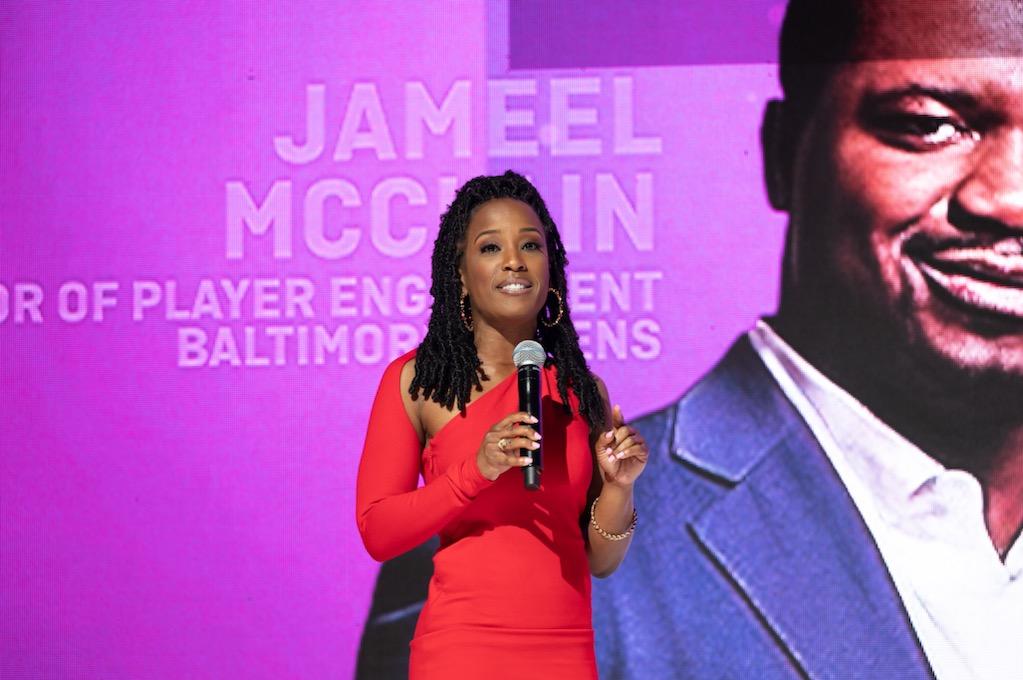 Megan Rivers speaking in a red dress at a Baltimore Ravens event with Jameel McClain on screen