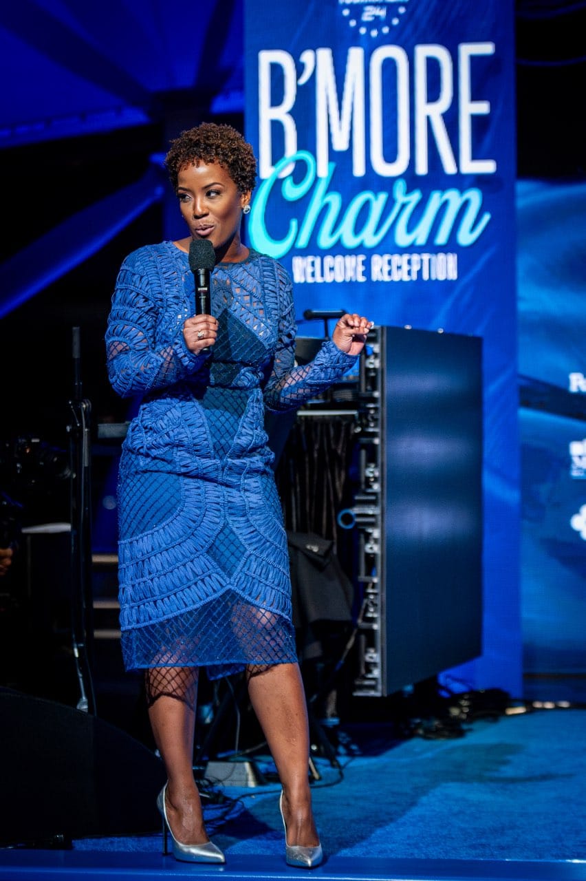 Megan Rivers speaking on stage with a microphone, looking out to the audience