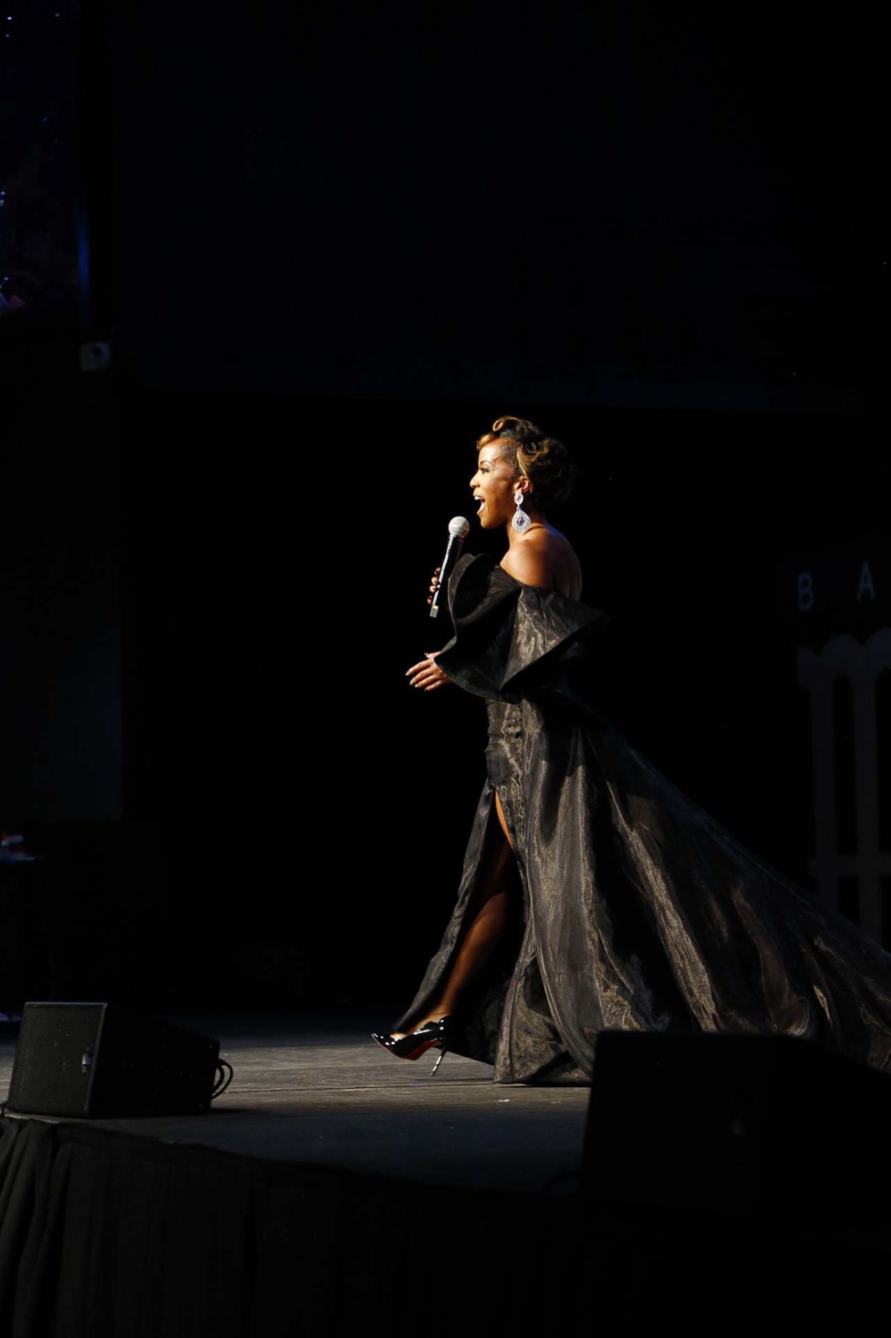 Megan Rivers speaking on stage in a black gown